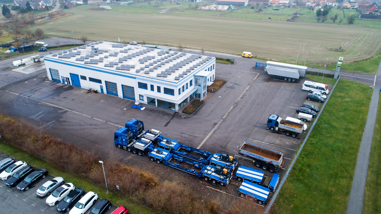 Luftaufnahme der Gewerbehalle mit Bürogebäude und Photovoltaik in Bechlin, davor Speditions-LKW