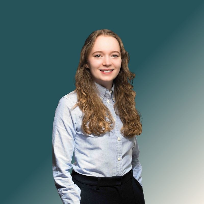 Lara Lubig, lächelnde Mitarbeiterin im hellblauen Hemd vor petrolfarbenem Hintergrund