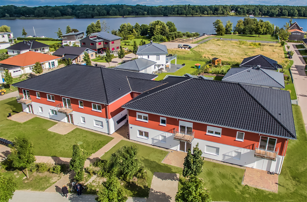 Moderne Wohnanlage Sonnenallee in Neuruppin aus der Luft, mit Seeblick und rotem Fassadenakzent